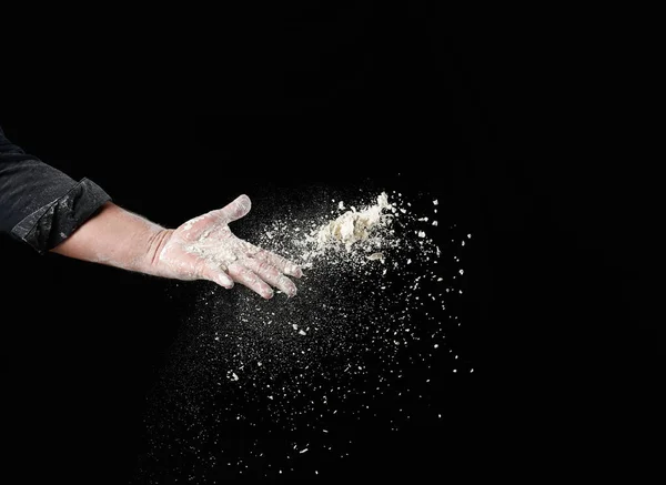 パン屋の男性の手は黒の背景に白い小麦粉の一握りを投げ 粒子は異なる方向に飛ぶ — ストック写真
