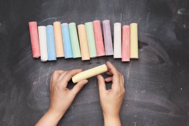 Siyah arkaplanda çok renkli tebeşir ve iki kadın eli, üst görünümde.