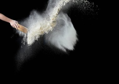 Kadın eli, beyaz buğday ununu siyah arka planda, yuvarlak bir ahşap elek aracılığıyla süzüyor, ürün dökülüyor.