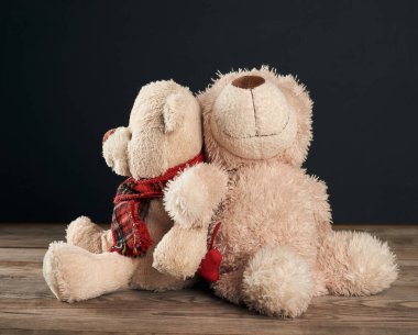 İki kahverengi oyuncak ayı kahverengi tahta bir masada oturuyor, siyah arka plan, aile kavramı.