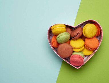 yuvarlak, çok renkli, kırmızı bir karton kutunun içinde yeşil bir arka planda kalp şeklinde uzanan makaronlar, üst görünüm, kopyalama alanı