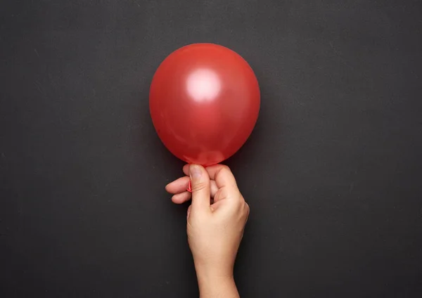 Weibliche Hand Die Einen Aufgeblasenen Roten Luftballon Auf Schwarzem Hintergrund — Stockfoto