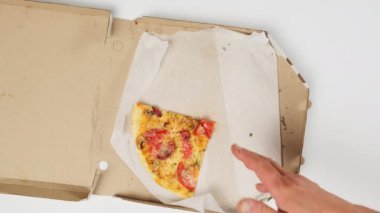 Kadın eli, erkeğin bir dilim lezzetli pişmiş pizzayı kağıt kutudan, beyaz masadan ve üst manzaradan sosislerle almasına izin vermez.