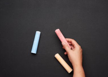 Boş bir kara tebeşir tahtasının arka planında kırmızı tebeşirle duran kadın eli.