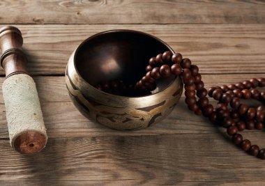 Kahverengi ahşap bir masanın üzerinde ahşap bir çırpıcıyla Tibet bakır kasesi, yakın çekim