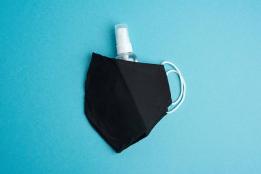 Tekrar kullanılabilir siyah tekstil maskesi, mavi arka planda dezenfektan şişesi, üst görünüm.
