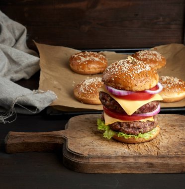 Domatesli duble çizburger, soğan, barbekü pirzolası ve eski bir tahta kesme tahtasında susamlı ekmek. Fast food, yakın çekim.