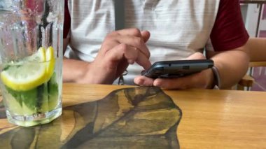 Yetişkin bir adam bir kafede bir masaya oturur ve akıllı telefon ekranına bakar, dokunmatik ekrana parmaklarıyla dokunur, internette sörf yapar.