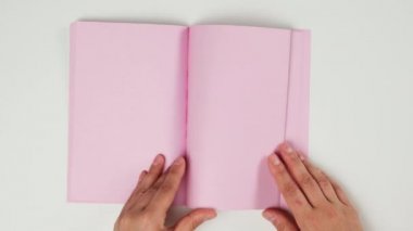 Beyaz masa üzerinde boş pembe sayfalar olan not defterini karıştıran kadın eli.
