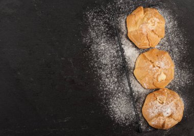 Kremalı pasta ve üzerine pudra şekeri serpiştirilmiş siyah tahta, üst görünüm, kopyalama alanı