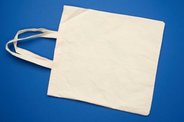 Mavi arka planda boş bej tekstil torbası, plastik torbaların reddedilmesi, düz konum, sıfır atık 