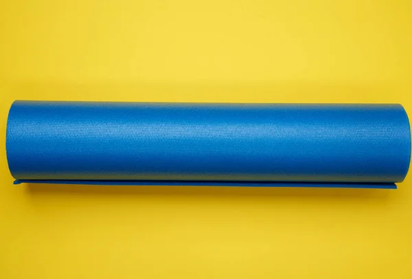 扭曲的蓝色氯丁橡胶垫 用于黄色背景的瑜伽和运动 顶部视图 — 图库照片