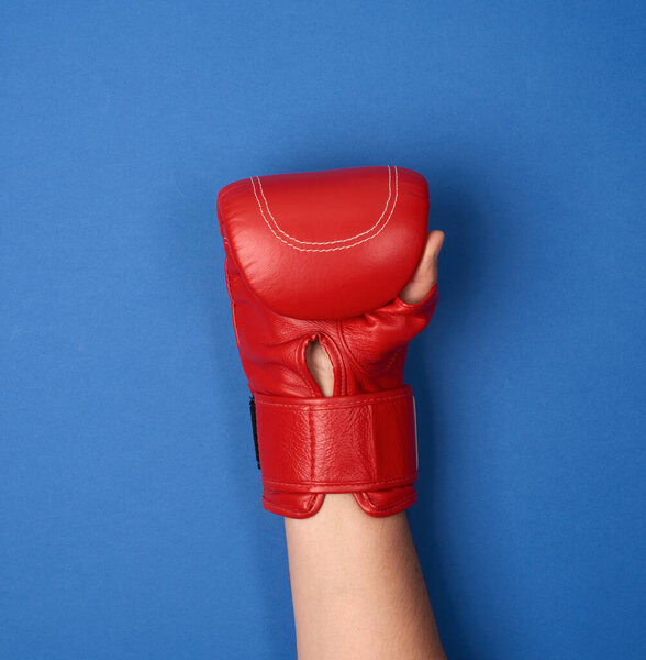 red leather boxing glove on a female hand on a blue background is raised up