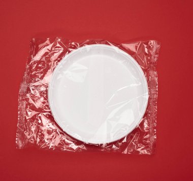 Kırmızı zemin üzerinde şeffaf plastik ambalaj içinde tek kullanımlık beyaz plakalar, üst görünüm