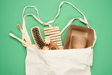 Beyaz tekstil çantası ve kahverengi el işi kağıdından tek kullanımlık sofra takımı, diş fırçası, yeşil arka planda tarak. Yukarıdan görünüm, plastik reddetme konsepti, sıfır atık 