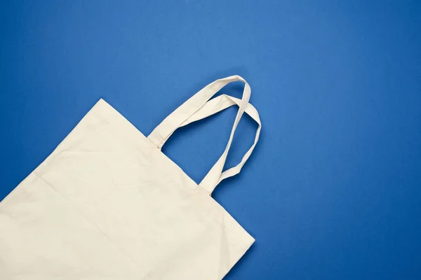 empty beige textile bag on blue background, rejection of plastic bags, flat lay, zero waste