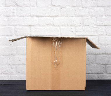 Beyaz tuğlalı arka planda kahverengi yuvarlak kartondan yapılmış boş dikdörtgen kutuyu aç, kapat