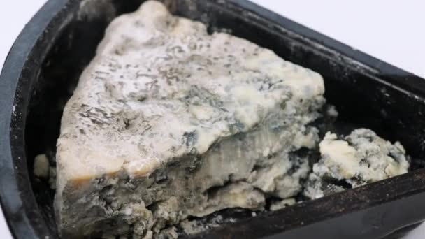白い背景の黒いプラスチック製の容器の中の青いチーズのスライス トップビュー 食べ物は回転します — ストック動画