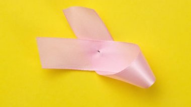 Sarı arka planda pembe kurdele, göğüs kanseri farkındalığı sembolü, üst görünüm.