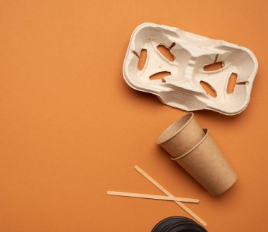Kahverengi el işi kağıdından tek kullanımlık kağıt bardaklar ve turuncu arka planda geri dönüştürülmüş kağıt tutucular, üst görünüm, plastik reddetme konsepti, sıfır atık 