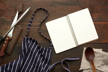 Kahverengi ahşap masa üzerinde boş beyaz çarşaflar ve mutfak gereçleri olan açık bir defter.