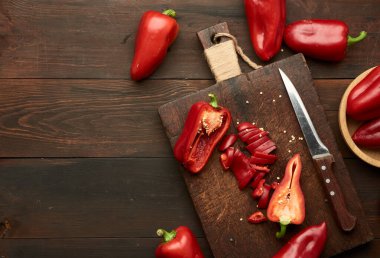 Tahtada dilimlenmiş kırmızı biber, kahverengi ahşap masa, üst manzara, kopyalama alanı