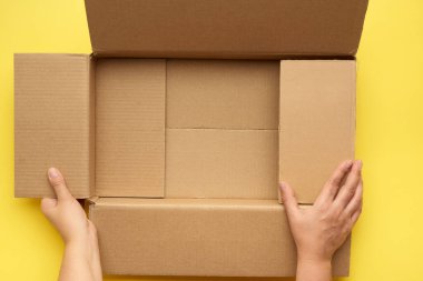 Kadın elleri boş bir kutu tutuyor. Kahverengi karton, üst görünüm, paketleme konsepti.
