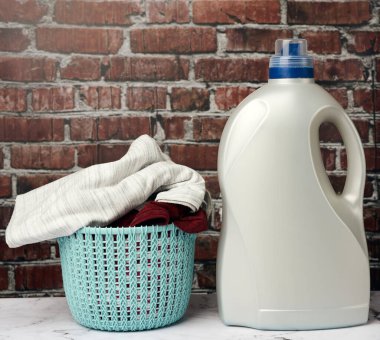 Plastik yuvarlak çamaşır sepeti ve kahverengi tuğlalı arka planda sıvı çamaşır tozu olan gri şişe.