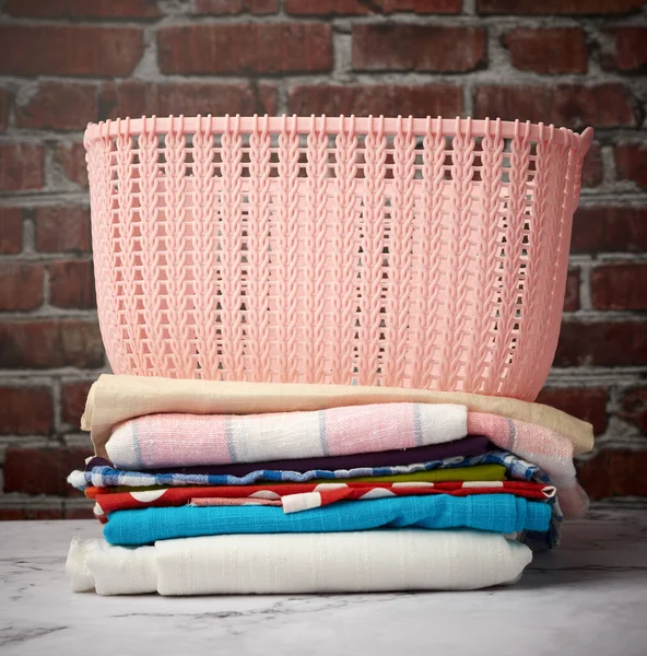 stack of folded laundry and empty laundry basket, brown brick wall background, close up