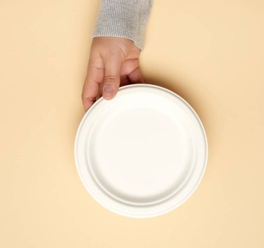 Bej arka planda tek kullanımlık beyaz kağıt plaka, üst manzara. Plastik ve çevre koruma kavramlarının reddi.