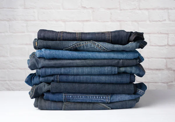 Beyaz tuğlalı arka plan karşısında katlanmış kot pantolon yığını, kapat