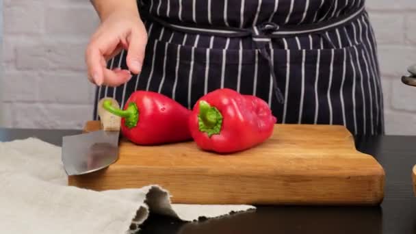 Femme caucasienne dans la cuisine empile des poivrons mûrs rouges entiers sur une planche de cuisine brune, gros plan