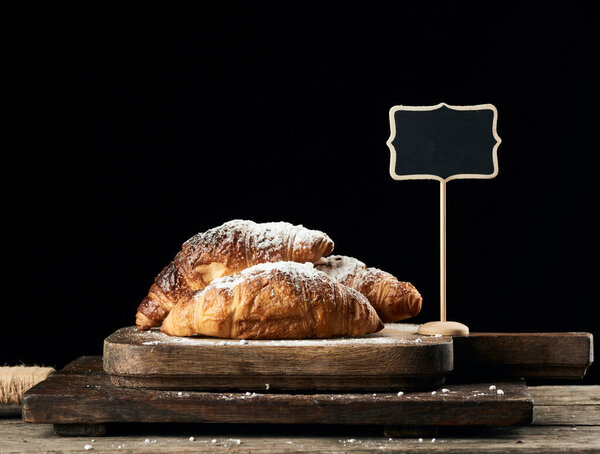 baked croissants on brown kitchen board, black background, wooden table