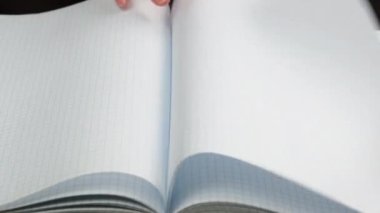 Bir kadının eli okul defterinin boş beyaz çarşaflarını kafese çevirir, kapatır.