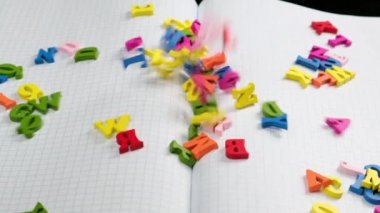 İngiliz alfabesinin rengarenk harfleri, yavaş çekimde, boş bir defter kağıdına düşüyor.