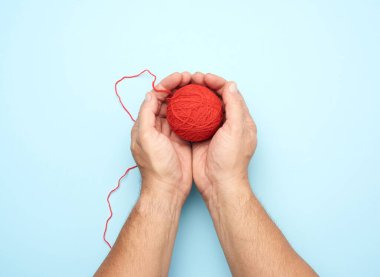 İki erkek el, kırmızı yün bir iplik topunu tutuyor, mavi arka plan, üst manzara.