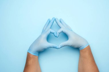 Mavi lateks steril eldivenli iki erkek el mavi arka planda kalbin bir jestini gösteriyor. İyilik, yardım ve gönüllü olma kavramı.