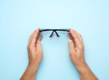 Mavi arka planda el ele tutuşan koruyucu plastik gözlük.