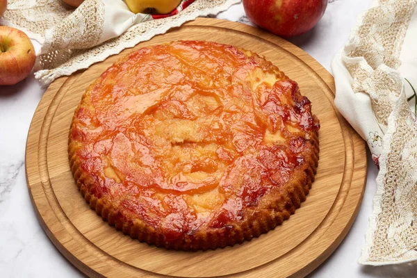 baked round apple pie on wooden board and fresh apples, top view, white table