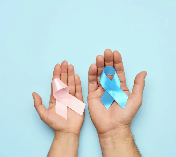 Pembe kurdele tutan kadın el, mavi kurdele tutan erkek el. Göğüs kanseri farkındalığı kampanyası konsepti ve prostat kanserinin tedavi ve mücadelesinin sembolü, üst bakış açısı