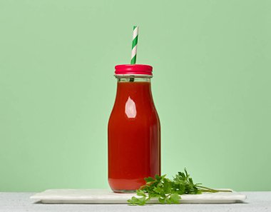 Domates suyuyla doldurulmuş ve yeşil çizgili kamışla süslenmiş kırmızı başlıklı cam şişe. Yeşil arkaplan