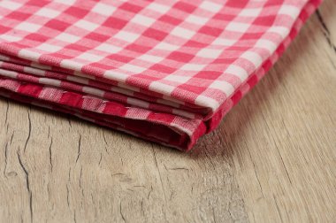 Ahşap bir yüzey üzerinde katlanmış kırmızı ve beyaz bir tekstil havlusu var..