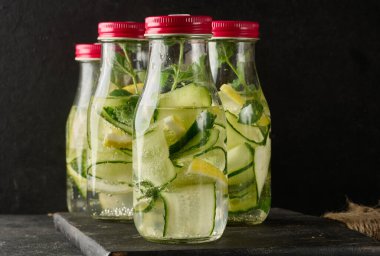 İçi salatalık, limon dilimleri ve nane yapraklarıyla dolu kırmızı kapaklı büyük şişeler.