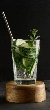 Bir bardak ferahlatıcı arınma suyu, salatalık dilimleri ve bir tutam nane, baloncuklu, koyu bir arka planda..