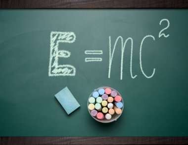 Kütle ve enerji arasındaki ilişkiyi ifade eden tebeşirle yazılmış bir denklem içeren bir okul kurulu. Yakınlarda bir sünger silgi ve bir fincan renkli tebeşir var..