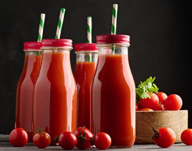 Koyu arkaplanda domates suyu ve olgun domateslerle dolu cam bir şişe.