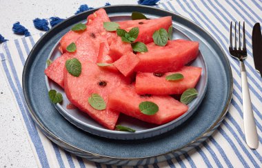 Parlak, sulu karpuz dilimleri ve bir tabakta servis edilen nane yaprakları. Üst görünüm.