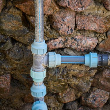 Büyük taşlardan yapılmış duvara monte edilmiş plastik su boruları.