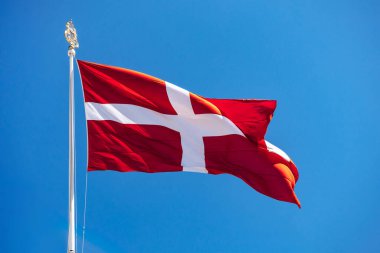 Malta Hükümdar Askeri Düzeni 'nin (Malta Emri) kırmızı ve beyaz bayrağının yakın çekimi açık mavi gökyüzüne doğru bayrak direği sallıyor.