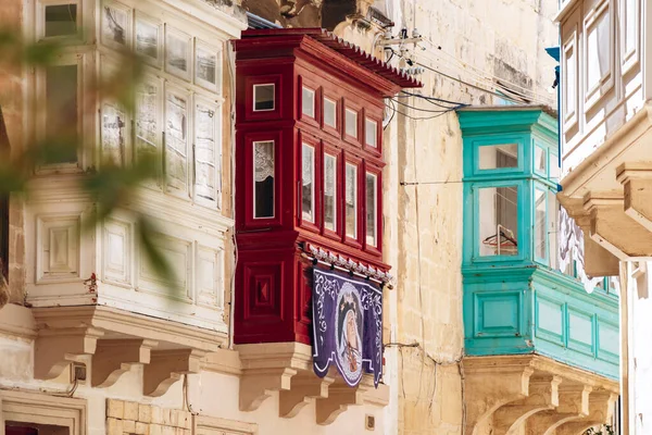 Beyaz, kırmızı ve turkuaz renklerde canlı geleneksel Malta balkonları, Senglea 'nın tarihi merkezinde kireçtaşı cephesinde dini bir pankart sergileniyor..